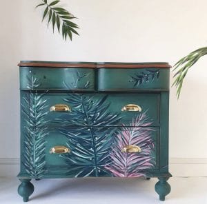 A dark green dresser with palm fronds painted in blues and purples.